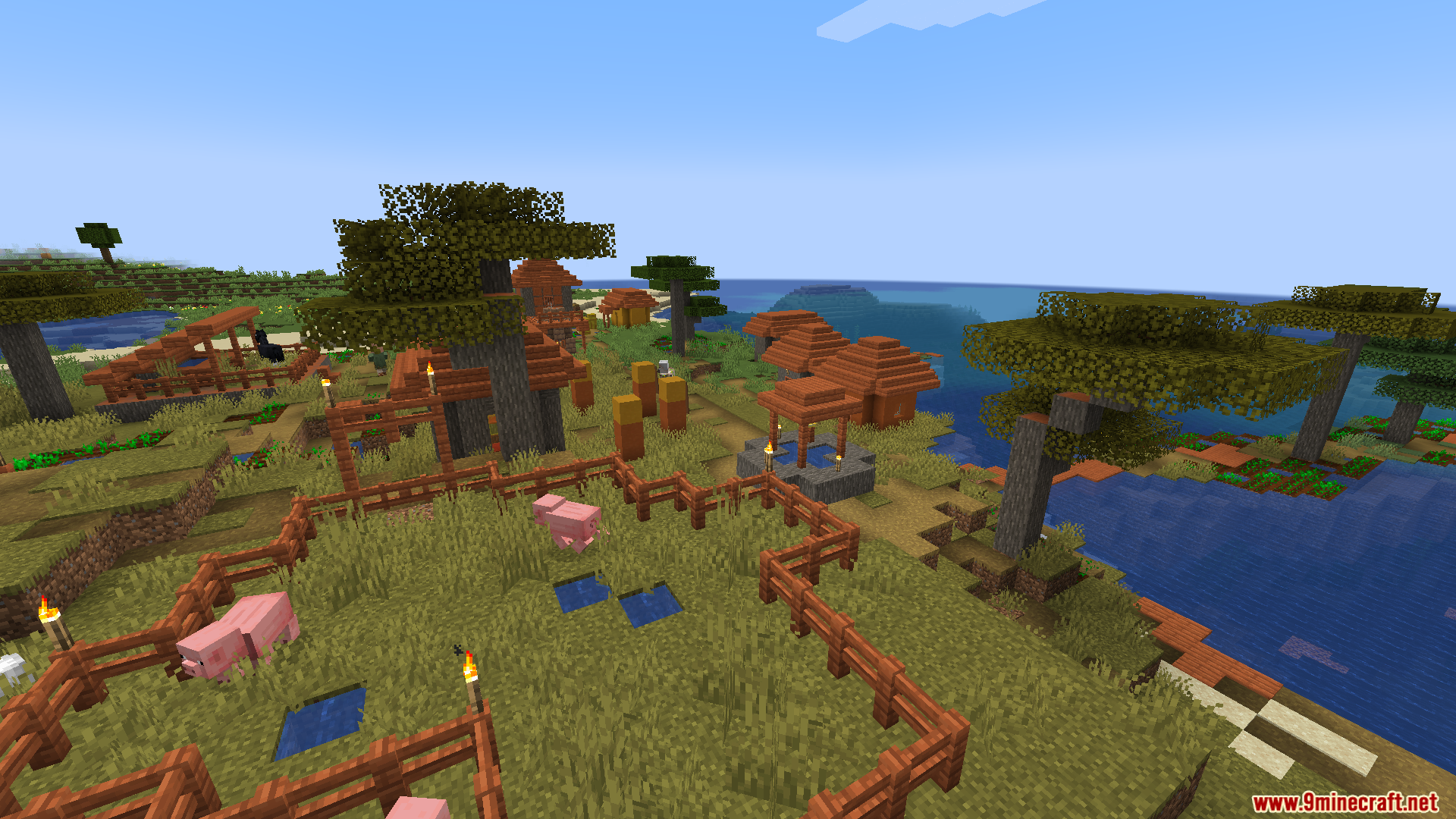 Pink pigs roaming inside a wooden enclosure within a scenic savanna village