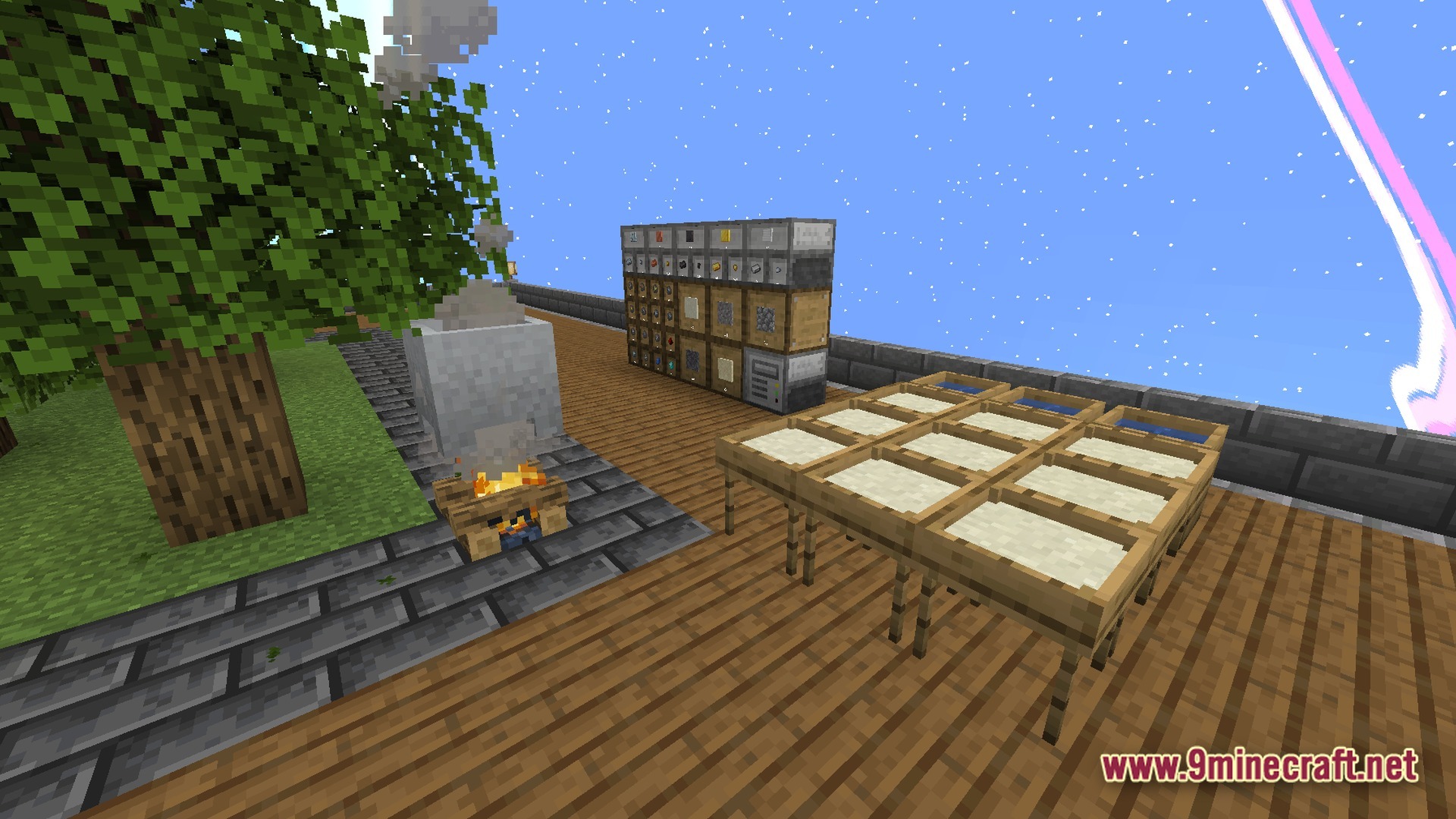 A campfire, stone cauldron, drying racks, and storage drawers on a wooden platform under a blue sky