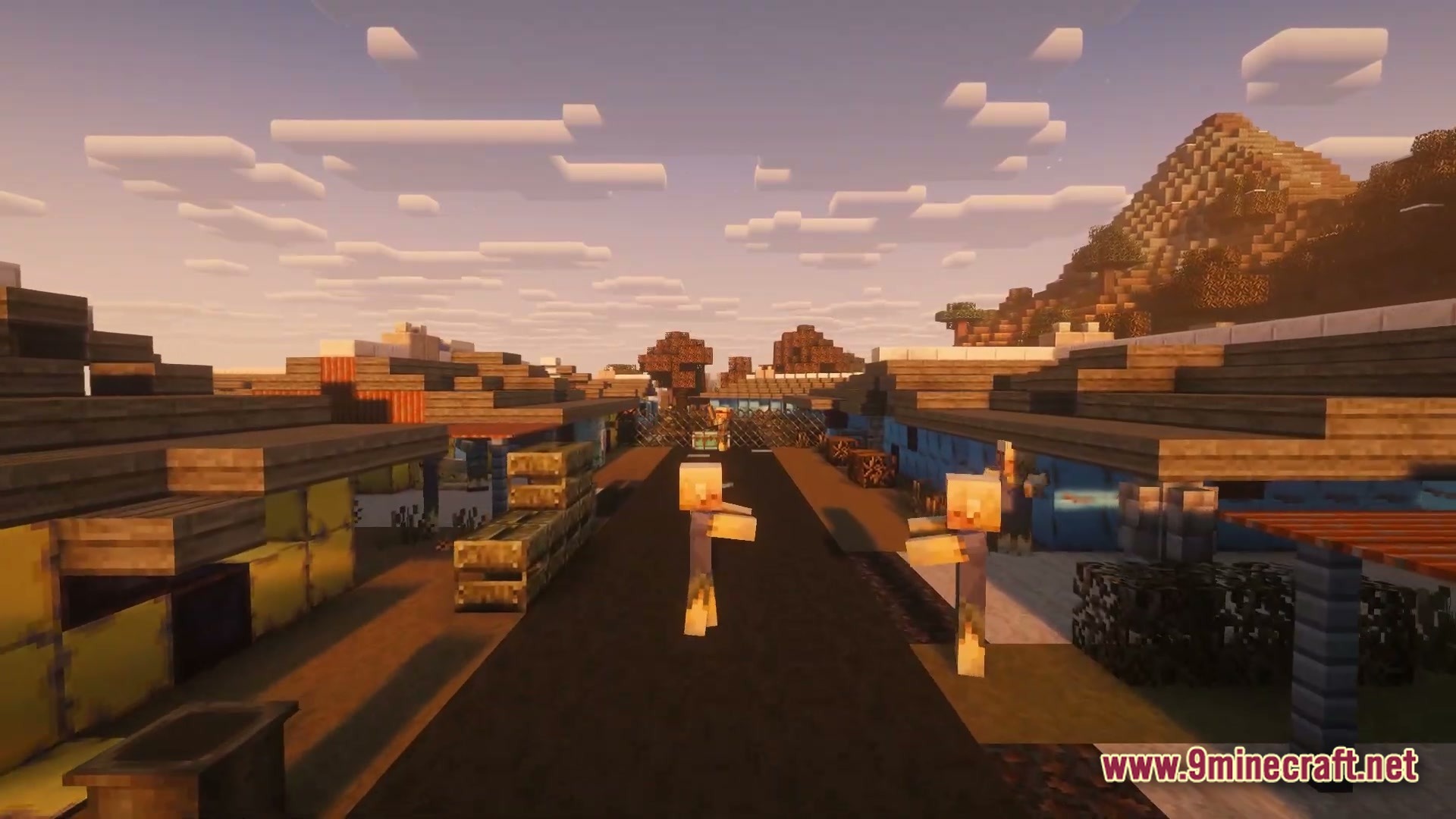 Zombies wander through a post-apocalyptic settlement with makeshift buildings and a paved road at sunset