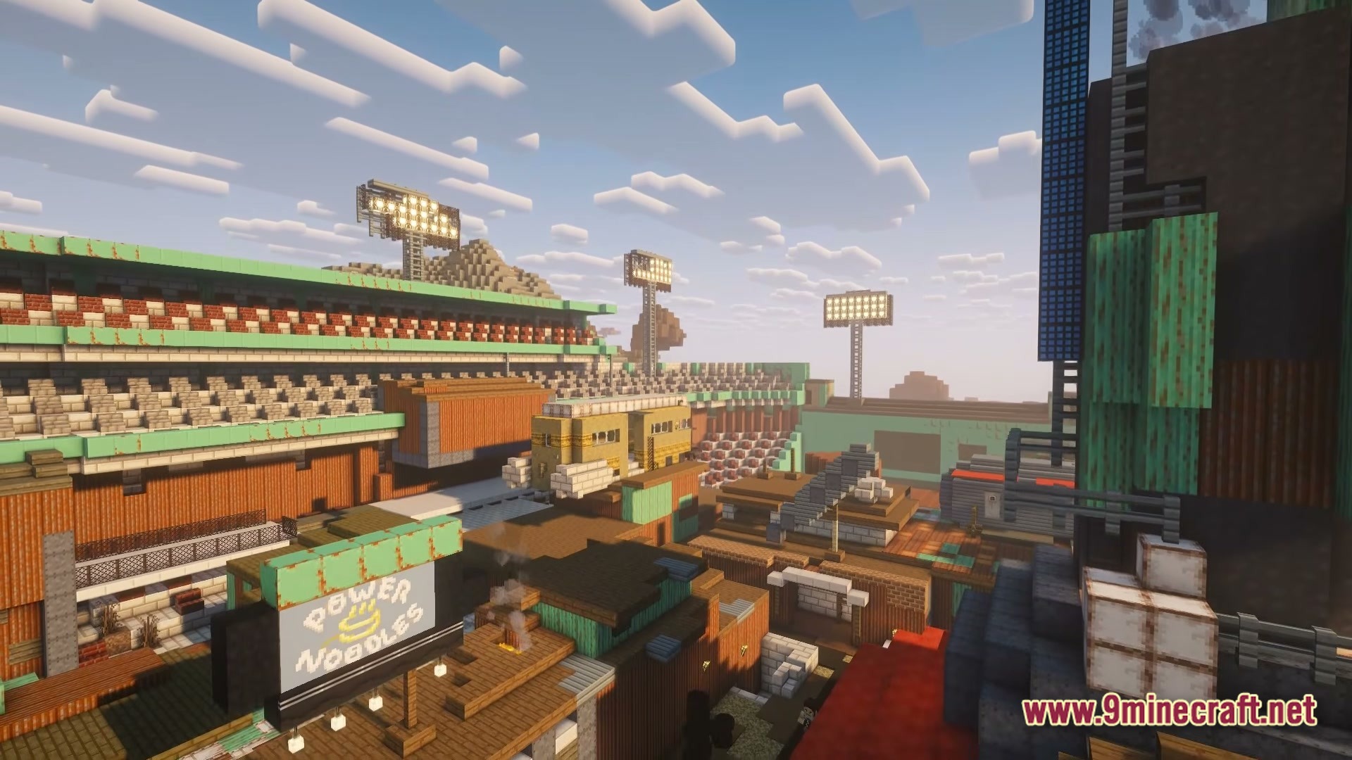 A post-apocalyptic settlement built within the ruins of a large sports stadium under a cloudy sky