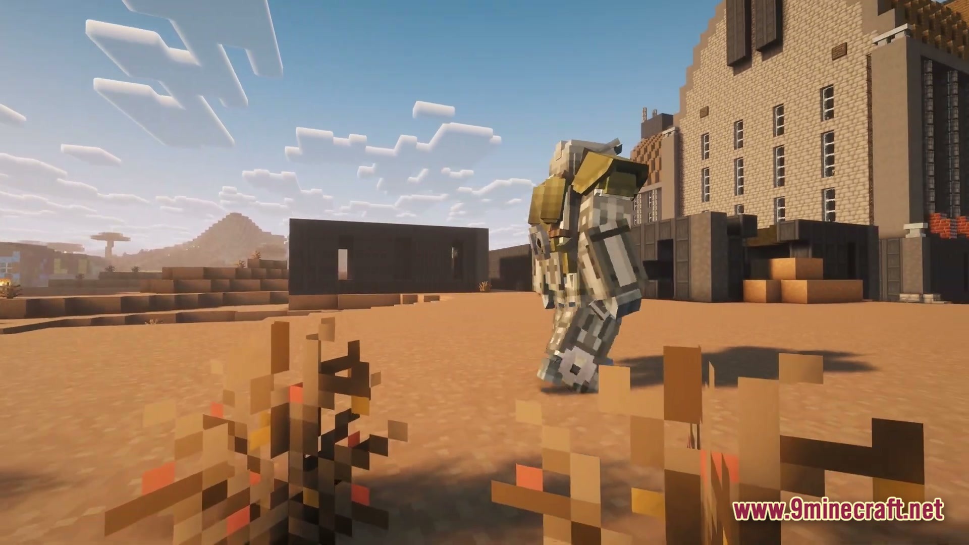 A player wearing heavy power armor walks through a desert wasteland near abandoned industrial buildings