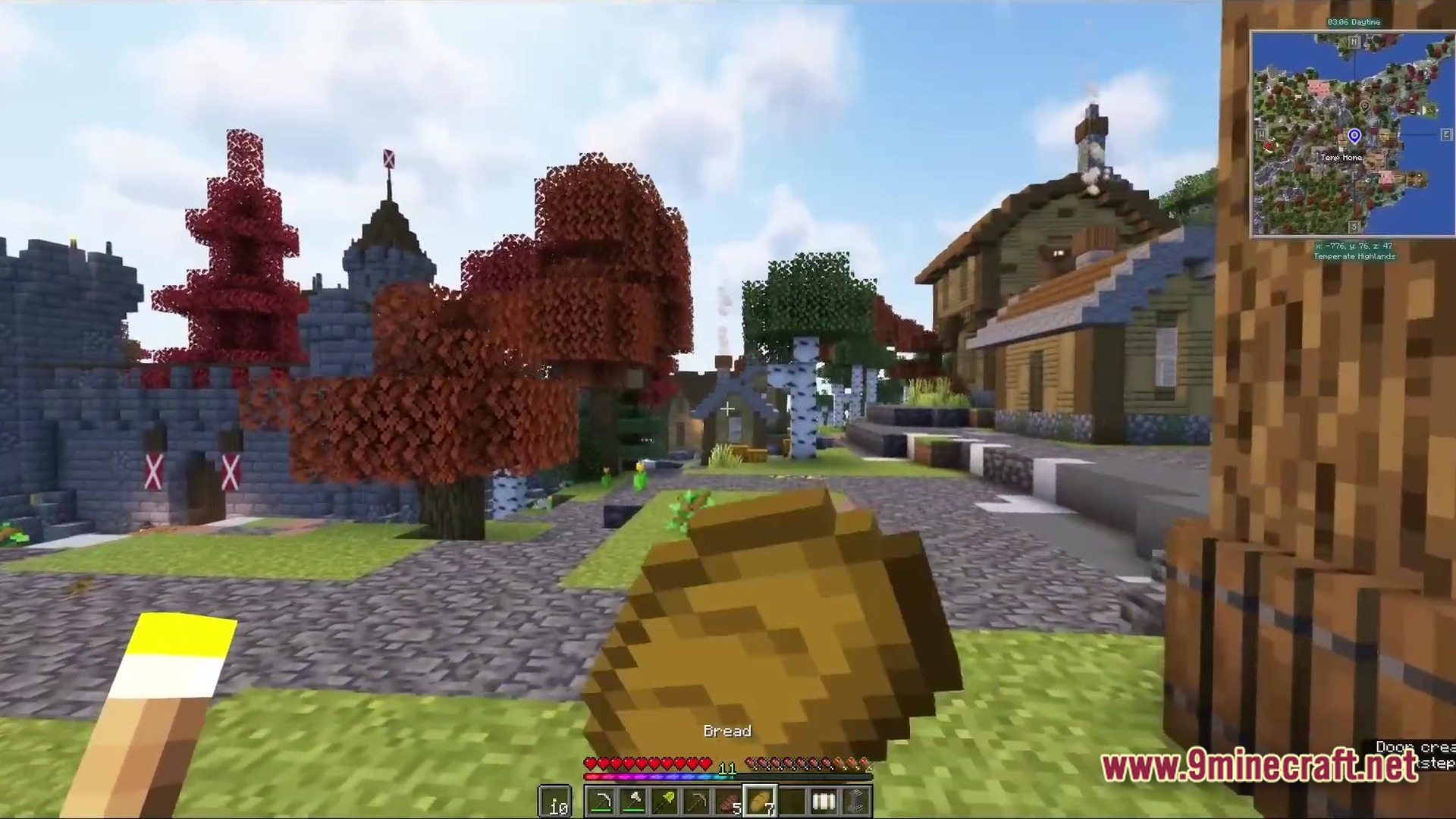 All The Mods 9 Atm9 Modpack (26.2, 1.20.1) – Craft The Ultimate Star 4 A player holds bread while standing in a village with custom houses, trees, and a stone castle