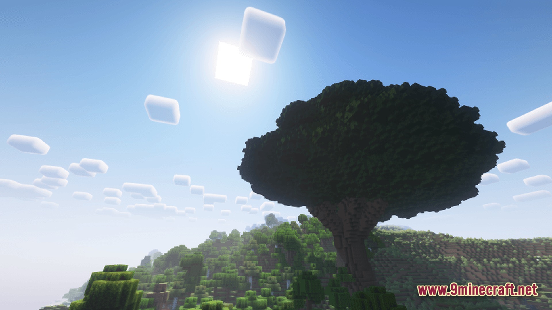 A massive greatwood tree stands prominently on a forested hillside under a bright, sunny sky