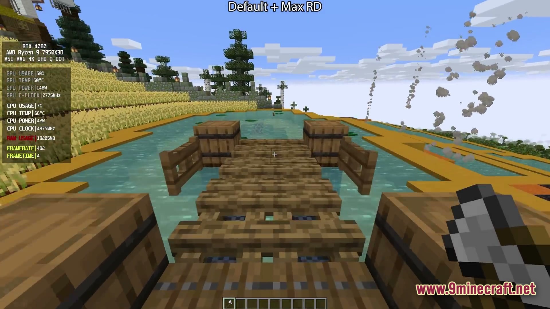 A wooden bridge with barrels extends over a pond near wheat fields and distant pine trees