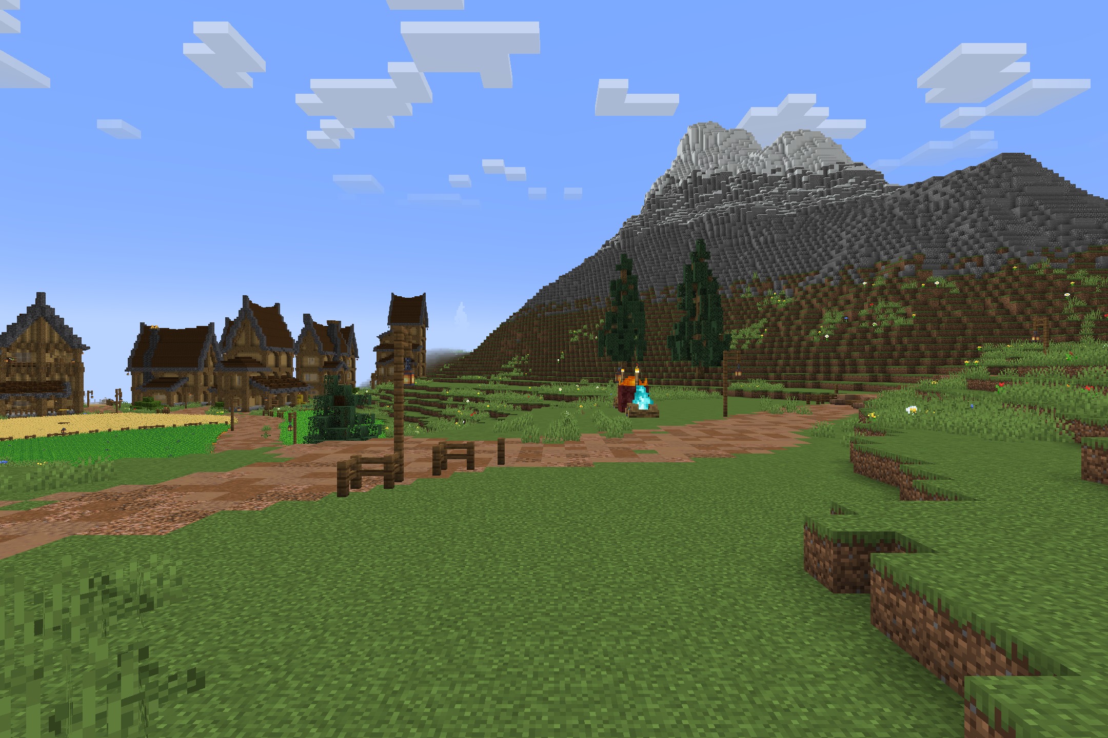 A village with wooden houses and a dirt path near a large mountain