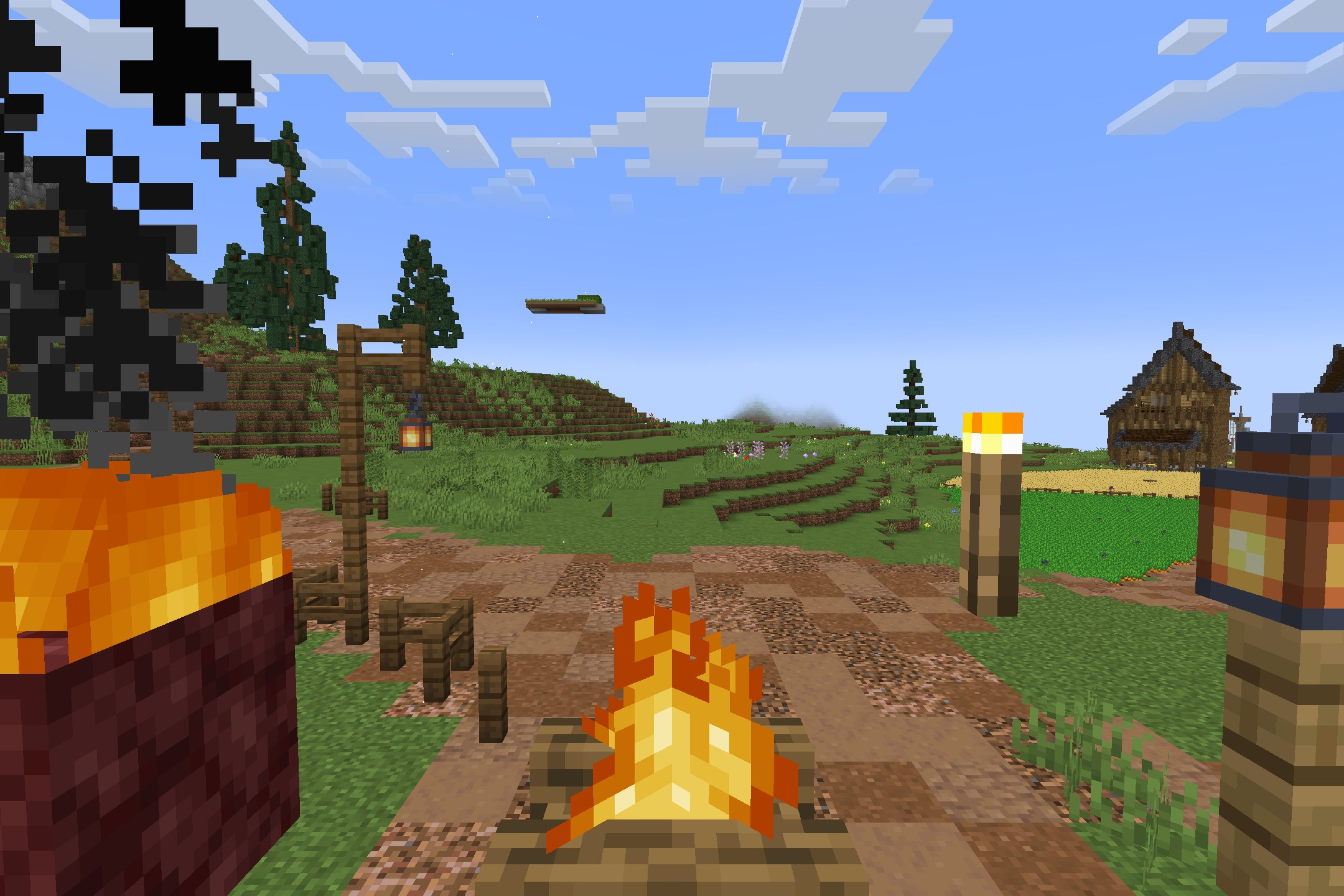 A campfire burns brightly in a grassy field near a wooden house