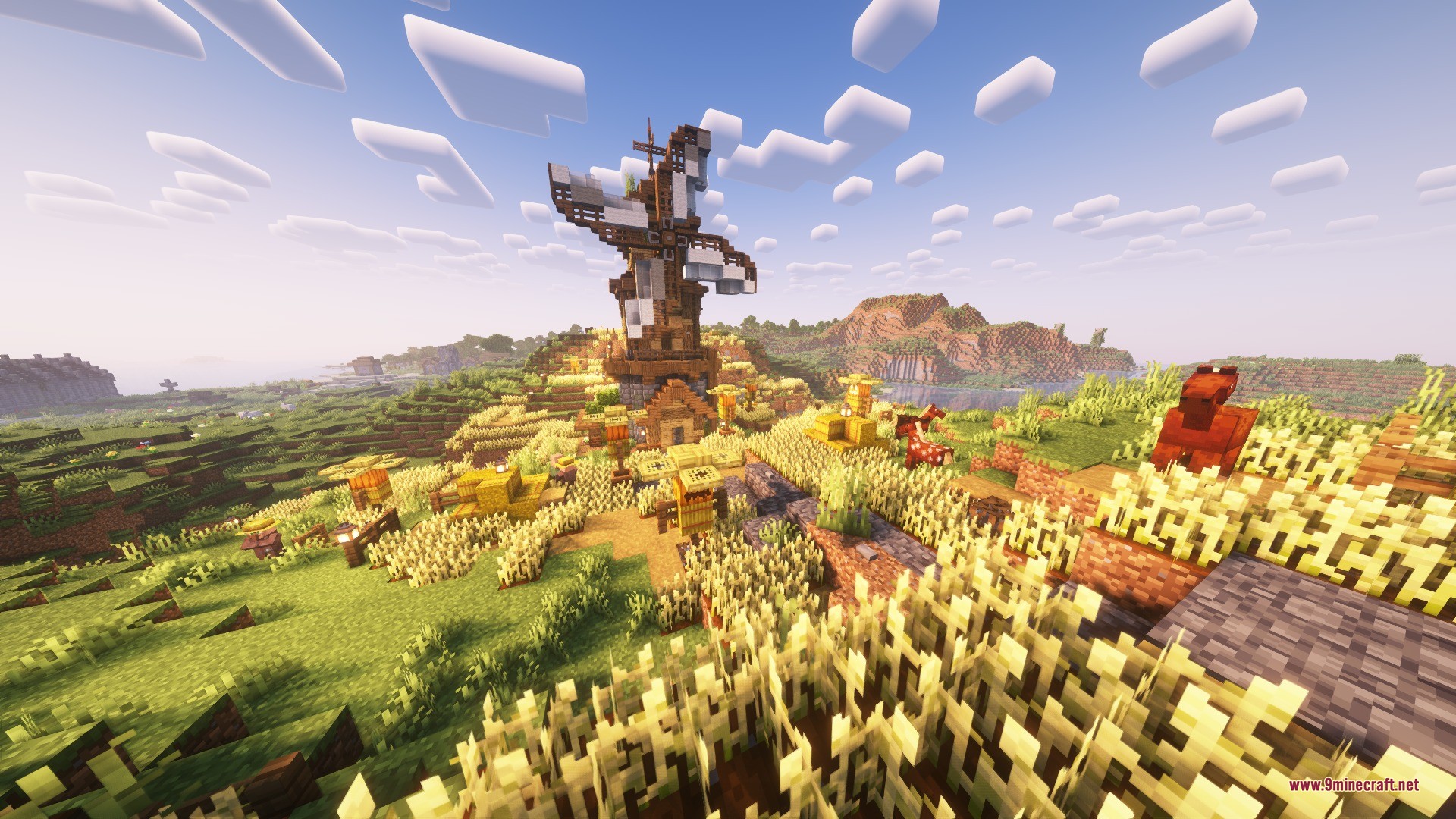 A large wooden windmill stands atop a hill surrounded by golden wheat fields