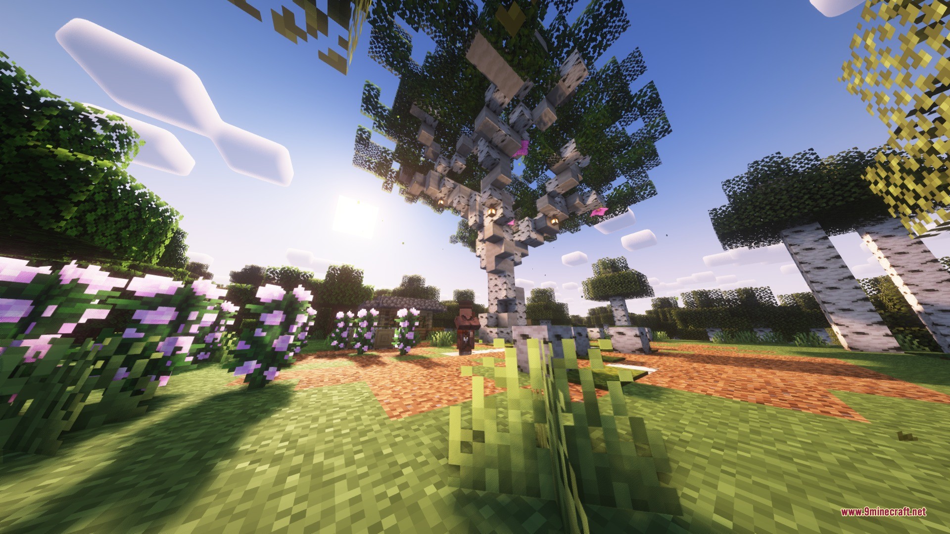 A massive custom birch tree with lanterns stands in a lush flower garden