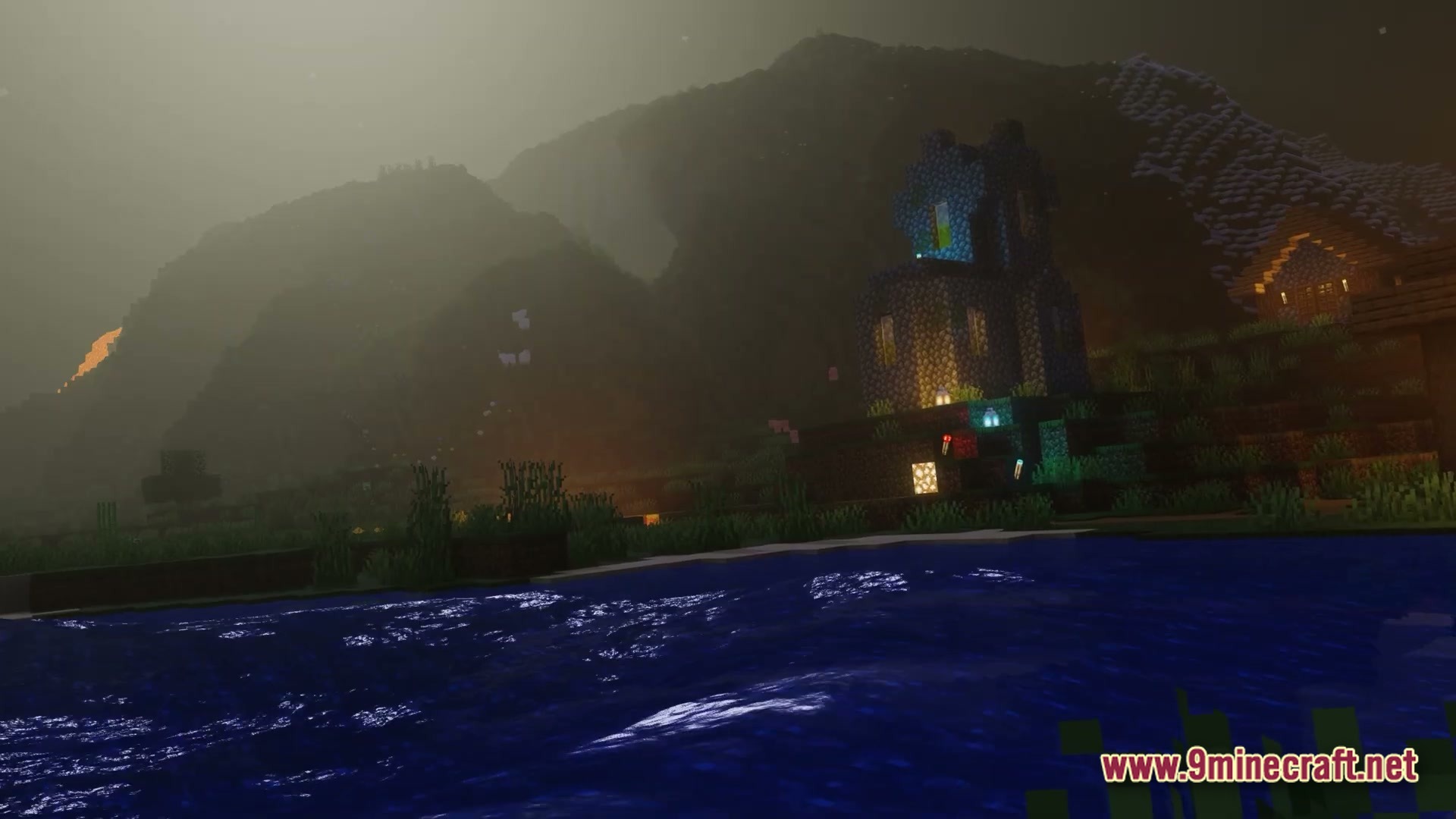 A cobblestone tower and house sit beside a river under a foggy, mountainous night sky
