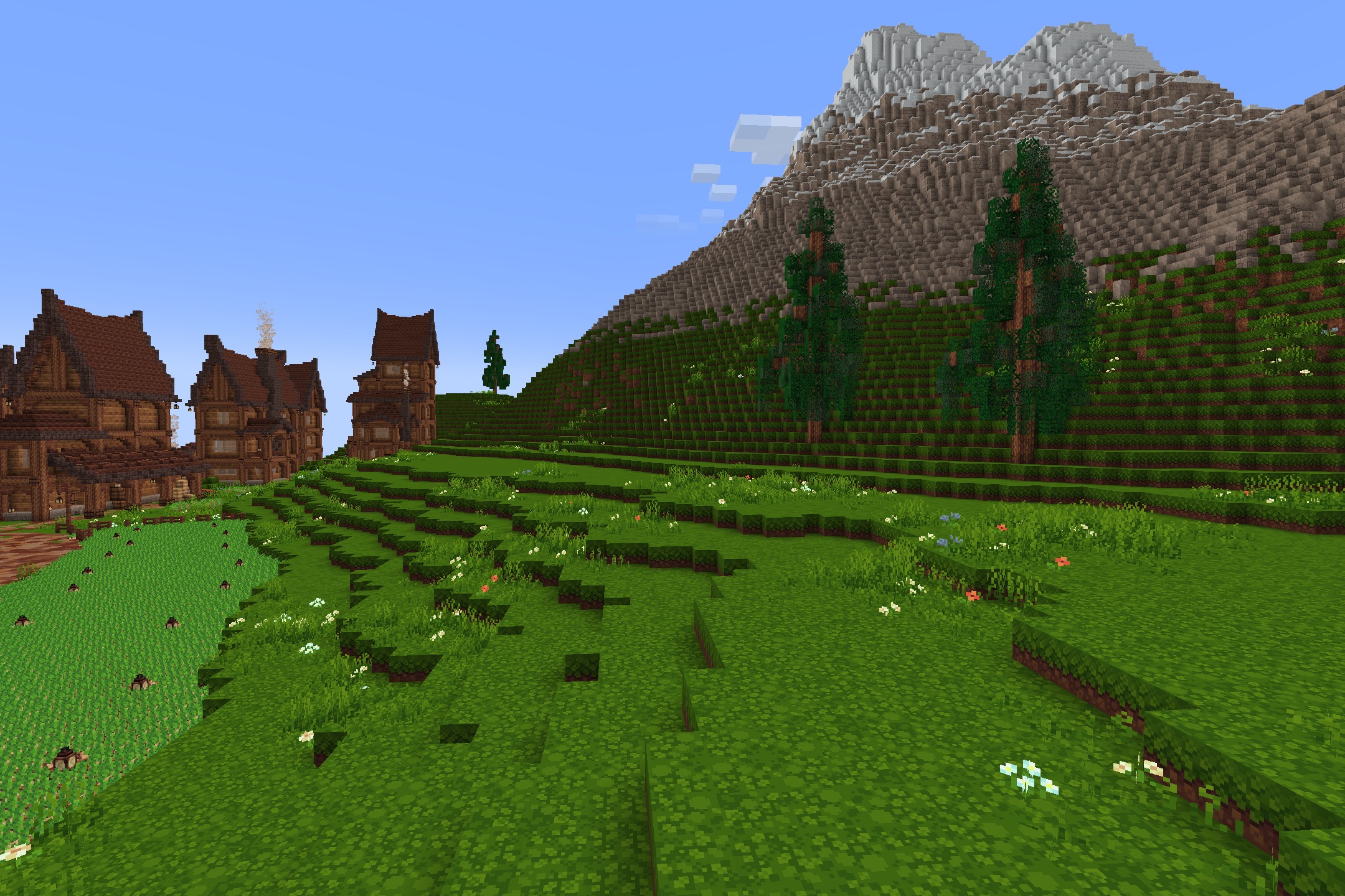 Lush green hills and tall mountains next to large wooden houses in minecraft