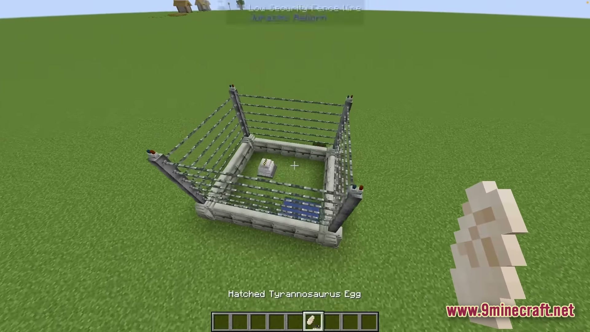 A small fenced enclosure containing a feeder and water source on a flat grass plain