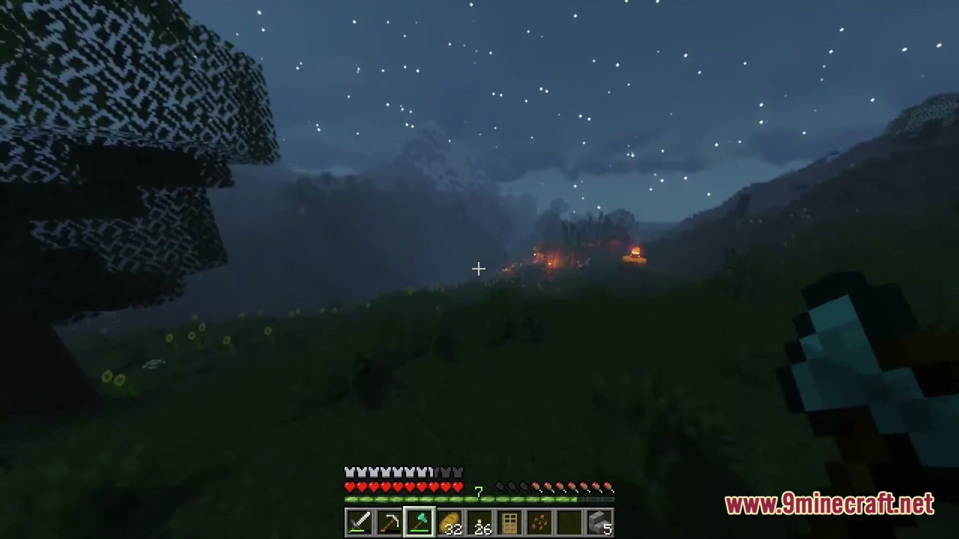 A player holds a diamond axe while looking toward a lit village under a starry night sky