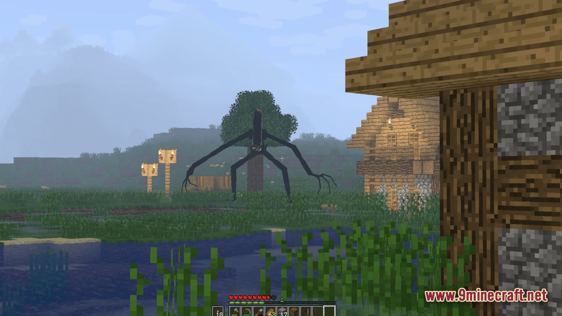 The Stalker Recreation Modpack (1.20.1) – Survive Craft Guns Hunt Monsters 8 A tall, dark, spindly creature stands in a field near a village under a foggy sky