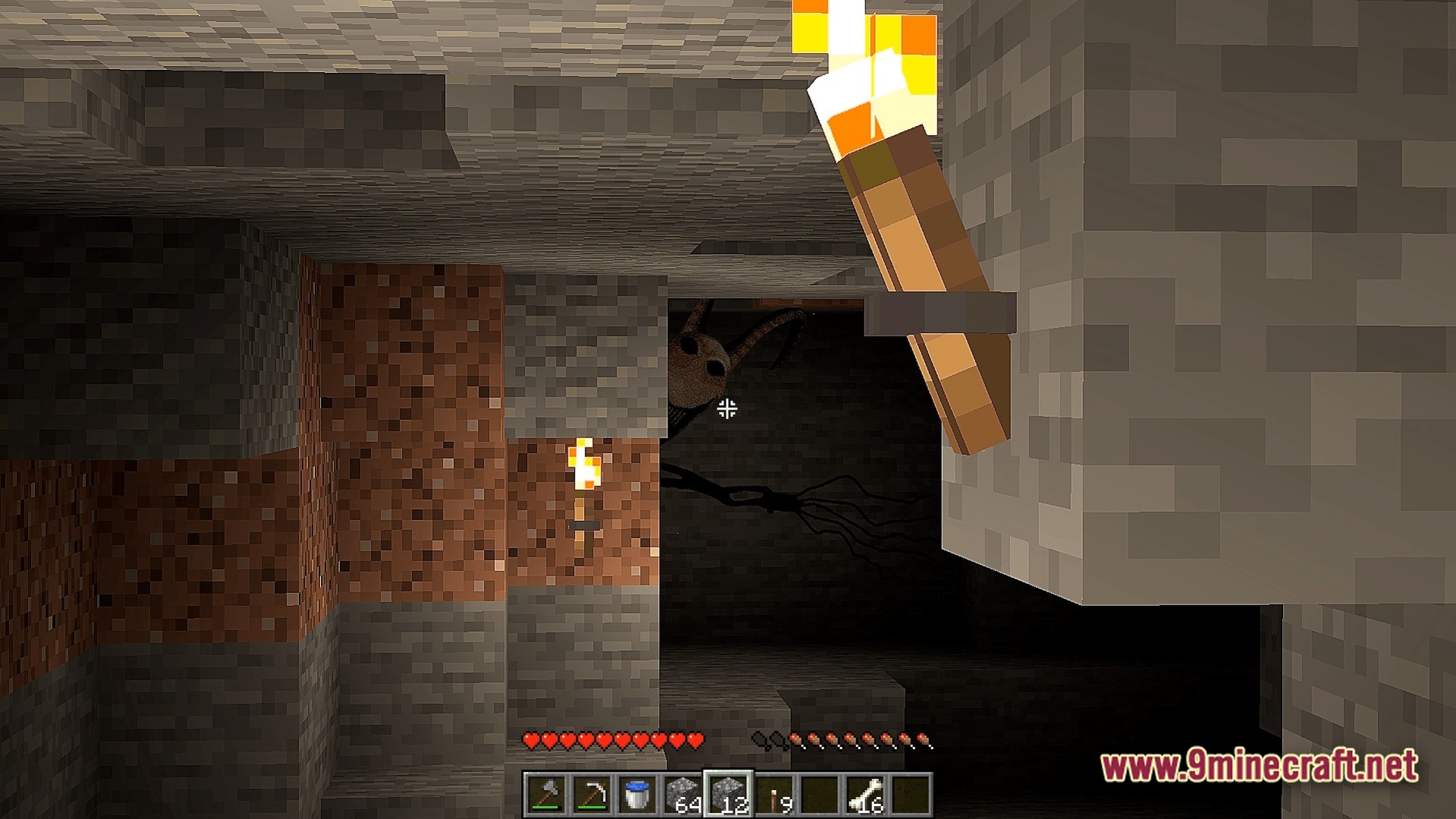 A tall, dark creature with large eyes peers around a corner in a dimly lit cave
