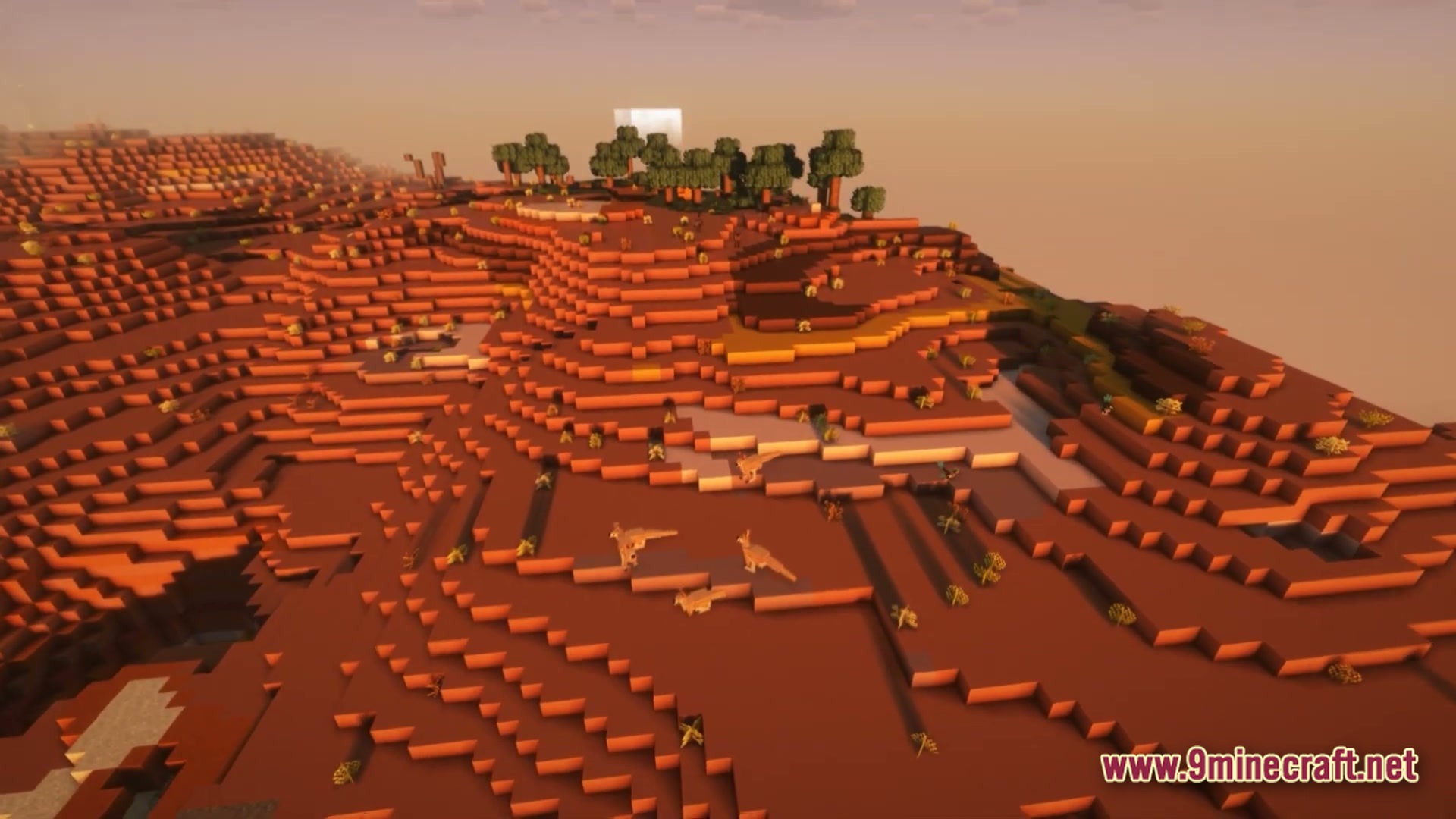 A group of dinosaurs wanders across a red desert mesa biome during a hazy sunset