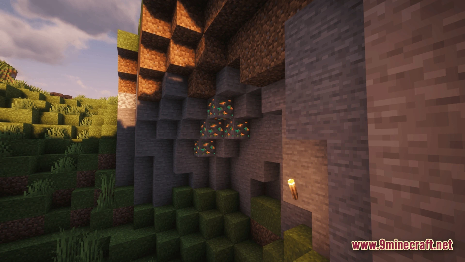 Copper ore blocks embedded in a stone cliffside next to a lit torch at sunset