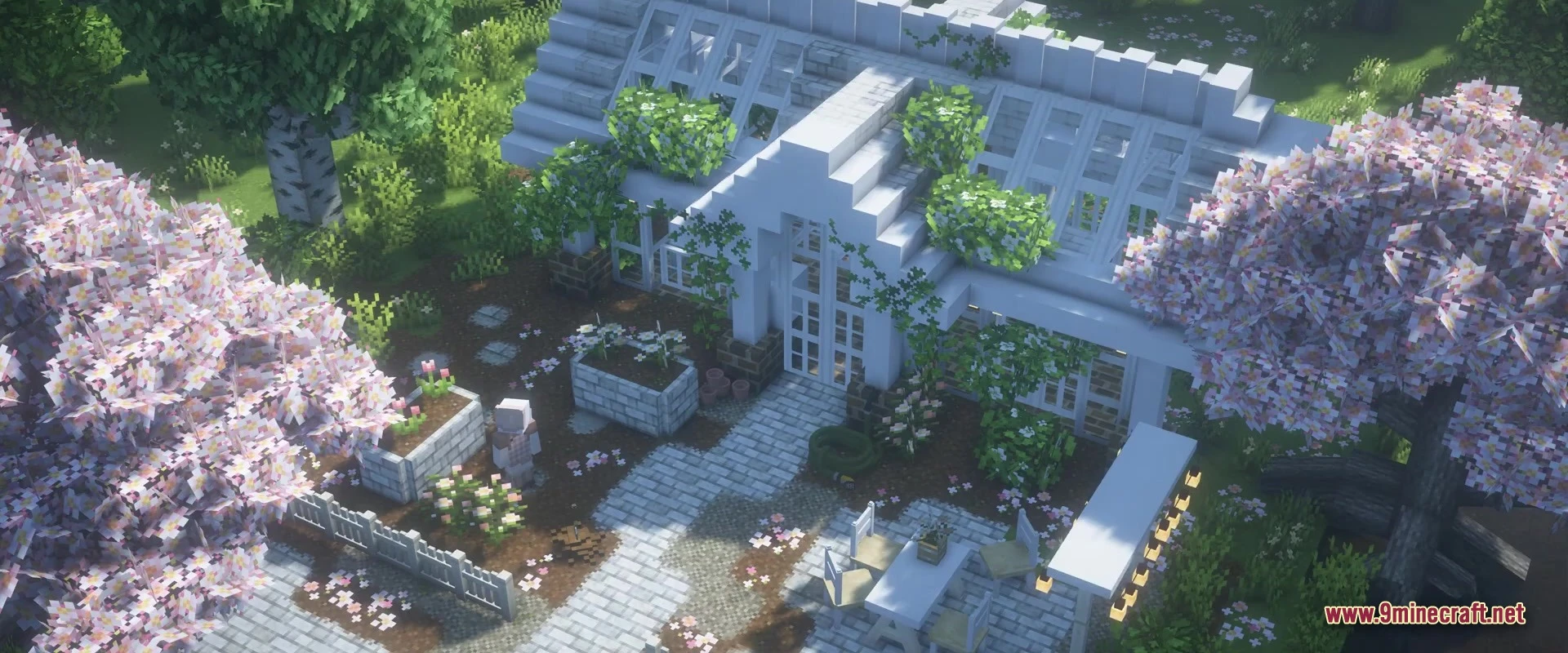 A white greenhouse surrounded by cherry blossom trees and stone paths in a garden