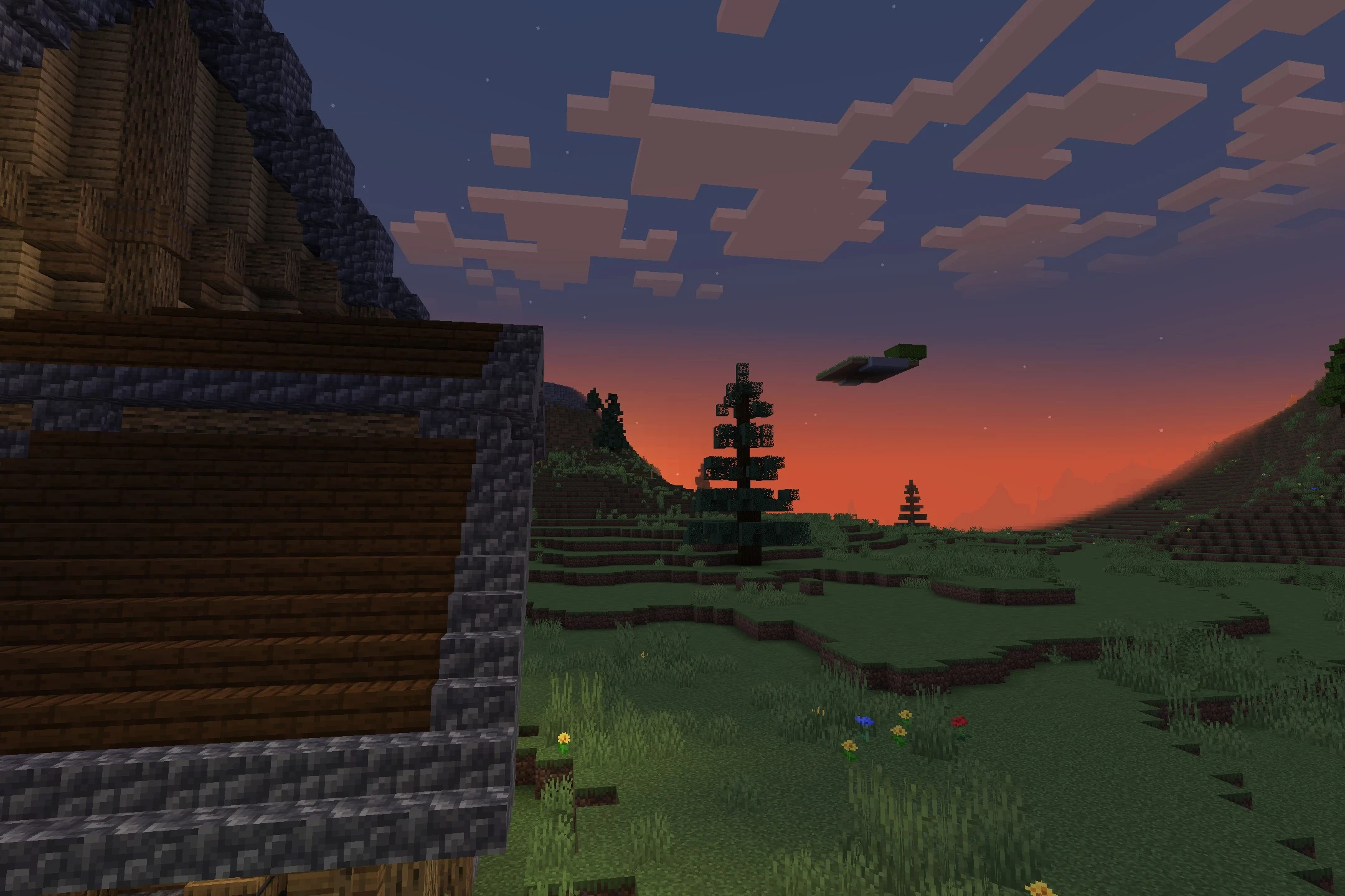 A grassy landscape with spruce trees and a wooden house during sunset